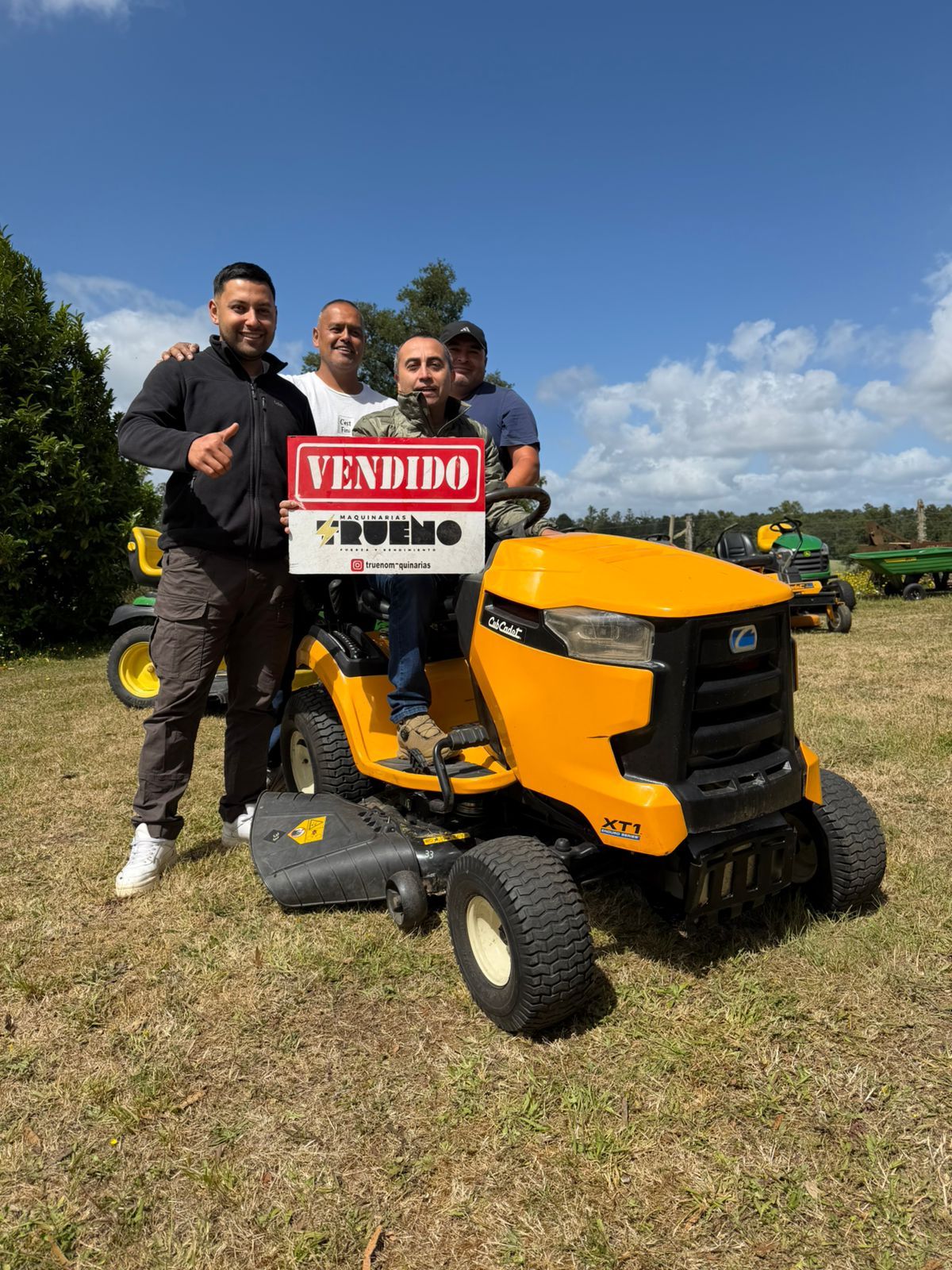 Clientes junto a un tractor cortacésped amarillo con un letrero de vendido.