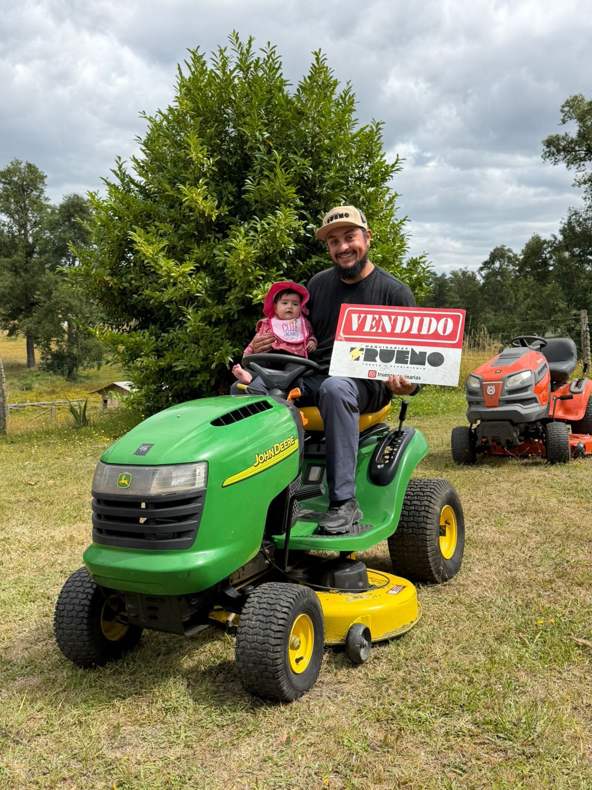 Clientes junto a un tractor cortacésped verde y amarillo con un letrero de vendido.