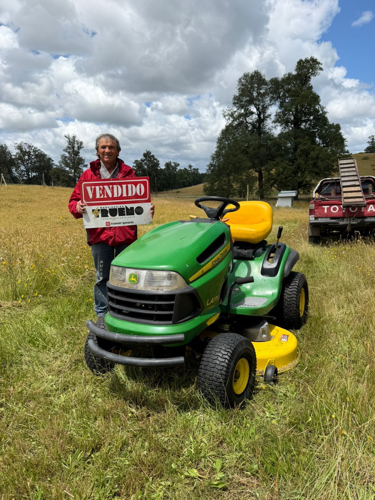 Cliente y tractor cortacésped verde con otros equipos al fondo.