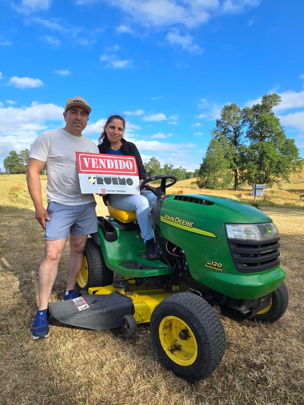 Clientes junto a un tractor cortacésped verde en un día soleado.