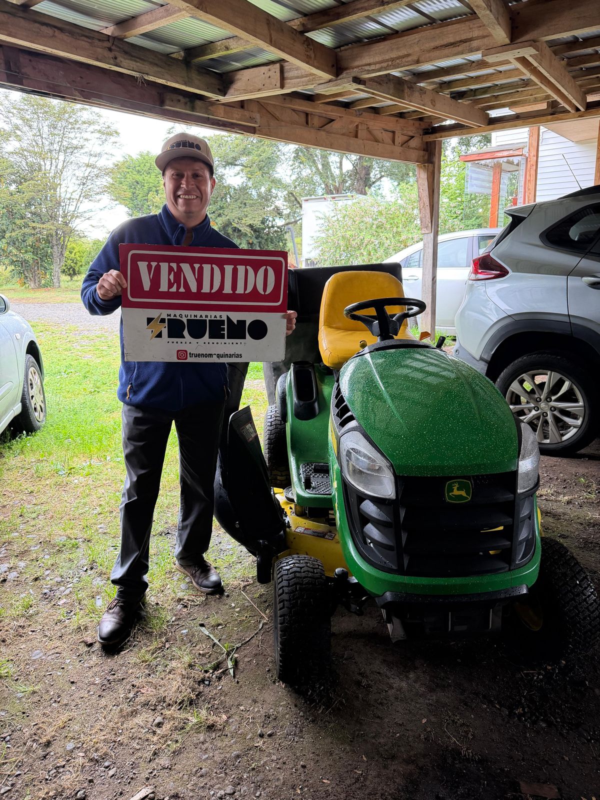 Cliente junto a un tractor cortacésped verde bajo un cobertizo.